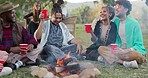 Friends camping at music festival with drinks, fire and happiness, freedom and fun at outdoor event. Nature, camp and group of people picnic at campfire, happy young men and women relax together.