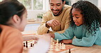 Family, father and children playing chess at a table while teaching and learning board game. Multiracial man and girl kids together at home for fun, play and competition for quality time and bonding