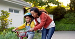 Mom, kid and teaching on bicycle outdoor in driveway of home for family support, help and play for childhood development. Excited mother, happy young girl and learning on bike for game, skill and fun