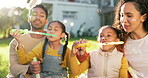 Kids, garden and a family blowing bubbles together outdoor during summer for fun while bonding. Mom, dad and happy children playing with a bubble wand in the backyard of their home during the day