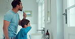 Father, child and brushing teeth in family home bathroom while learning or teaching dental hygiene. A man and kid with toothbrush and toothpaste for health, cleaning mouth and wellness at mirror