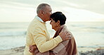 Senior couple, love and kiss at the beach for care, commitment and adventure outdoor. A man and woman embrace in retirement for freedom, peace and wellness on holiday, travel or vacation on cold day