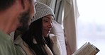 Woman reading a story while on a camp with her boyfriend in the outdoor forest or woods. Adventure, calm and couple sitting and relaxing in caravan enjoying a book or novel together on weekend trip.