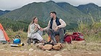 Couple, camping and fire with wood, coffee and relax in mountains, nature or forrest for holiday. Man, woman and campfire on ground for cooking, giving thermos and vacation in bush, field or morning