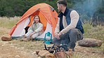 Couple, camping and outdoor with fire, talking and phone call to relax in woods, nature or forrest on holiday. Man, woman and cellphone in tent for chat, cooking or vacation in bush, field or morning