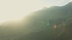 Mountain, landscape and sunrise in nature, morning or outdoor with field, grass or sky with clouds. Earth, drone view and lens flare with sunshine, blurred background or summer in natural environment