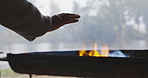 Hands, camping and fire with a person in the forest, getting warm by a bbq for heat while outdoor in the wilderness. Hiking, travel and an adult in nature to camp with a burning flame for survival