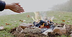 Camp, fire and hands in nature to relax in outdoor for travel on weekend with grass in closeup. Flames, camping and burning wood with person in environment for vacation for bonfire for survival.