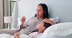 Mother taking care of her sick child in bed checking for a fever with a thermometer at home. Illness, stress and worried mom sitting with her girl kid with a cold, flu or allergies in the bedroom.