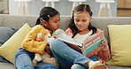 Sisters, together and reading a book on sofa for education or knowledge with literature in home. Kids, couch and learning for literacy with children or story telling for fantasy with care or love.