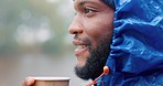 Camping, winter and a black man drinking coffee in the rain while outdoor in nature to relax. Hiking, morning and a young male tourist in the forest or woods for travel and freedom with a cup of tea