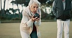 Senior woman, bowling and park on grass for sport, fitness and games for competition, health or fun. Elderly people, metal ball and lawn for contest, funny laugh or workout with blowing for good luck
