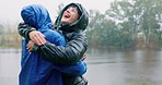 Camping, love and a couple hugging in the rain while outdoor in nature together for romance or adventure. Smile, freedom or travel with a man and woman bonding while hiking in wet winter weather