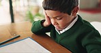 Bored, education and boy child doing homework, assignment or project in the dining room at home. Tired, sleepy and little kid student working on school work with books by the table of a modern house.