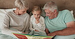 Bedroom, book and grandparents reading to a grandchild while in their home to relax together at a sleepover. Love, children and storytelling with a girl in bed, bonding with granny and grandpa