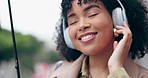 Happy woman, headphones and listening to music with umbrella in rain, city or outdoor audio streaming. Excited female person walking in relax with headset for sound track and dancing in an urban town