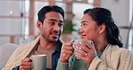 Coffee, happy and couple with blanket on sofa for bonding, relax and cozy in living room with fire. Love, dating and Asian man and woman with hot drink in conversation, talking and speaking at home