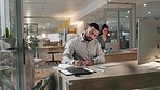 Computer, strategy and a business man writing in his notebook while planning in the office at night. Database, information and a young employee working at his desk in the workplace for research