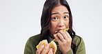 Young woman, eating burger and studio with face, french fries or comic for greed by white background. Japanese girl, student and fast food with bad choice for health, sandwich or portrait with chips