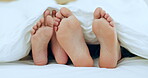 Couple, feet and relax in bed together on holiday, vacation or sleeping in the morning with love, comfort and playful touching. People, care and playing with foot under blanket in bedroom or home