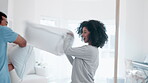 Pillow fight, interracial couple and happy in bedroom for love, energy and funny games together at home. Young man, excited woman and laughing with cushion for battle, crazy morning and silly play 