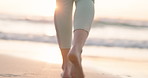 Beach, sunset and legs of person walking, travel and relax with ocean water, sand and foot steps on holiday break. Nature wellness, sea waves and barefoot feet of closeup tourist for outdoor freedom