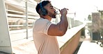 Sports, man and drinking water in city for fitness break, exercise and workout with headphones. Thirsty indian runner, bottle and hydration for energy, healthy recovery and listening to music outdoor