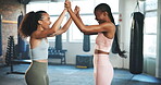Women, fitness and high five in gym for training and exercise teamwork, support and celebration or motivation. Young athlete, sports people and personal trainer with hands together for workout goals