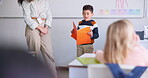 Child, student and reading a book in class for learning, development and communication. Boy kid and woman teacher for language, support and assessment or confidence in elementary classroom at school