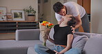 Kiss, gift and couple with flowers on a living room couch in a home as love, care and romantic bonding together. Present, spoil and man giving woman bouquet to celebrate anniversary in an apartment