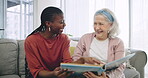 Photo album, assisted living and a happy senior with her black woman caregiver on a sofa in the living room. Smile, funny and elderly resident laughing at a memory with a nurse in a retirement home