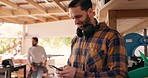 Carpenter man, phone and texting in workshop with reading, thinking or contact for networking. Entrepreneur handyman, smartphone and smile for email, notification or deal in industrial small business