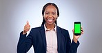 Happy black woman, phone and green screen with thumbs up on mockup against a grey studio background. Portrait of business African female person with like emoji, yes sign or OK for smartphone approval