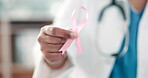 Hand, healthcare and a pink ribbon for breast cancer with a doctor in a hospital closeup for support or empathy. Medical, hope and awareness month with a confident medicine professional in a clinic