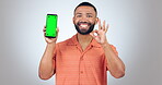 Phone, green screen and man with okay, yes and success hands for social media app or marketing in studio. Face of person on mobile mockup and certified or emoji, tracking marker and white background