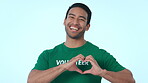 Smile, heart and a volunteer man pointing at you on a blue background in studio for love, charity or support. Portrait, vote and choice with a happy young community service worker selecting an option