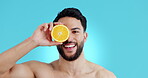 Face, orange and skincare smile with a man on a blue background in studio for natural beauty. Portrait, fruit or food and a happy young model with citrus for heath, nutrition or antiaging treatment