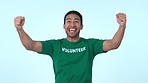 Volunteer, celebrate success and man in studio for community service, help and donation. Yes, excited asian person and volunteering with support, happiness and charity achievement on blue background
