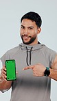 Happy man, personal trainer and phone with green screen, mockup or sign up against a studio background. Portrait male person pointing to technology display in fitness, advertising or join membership