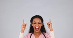 Medical doctor, pointing up and woman in studio with mockup space, advertising or promotion. Excited female healthcare worker on grey background for announcement, medicine and hand or banner portrait