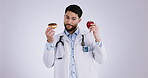 Face, man and doctor with a cupcake, apple and healthcare options on a white studio background. Portrait, medical professional or person with dessert, fruit and diet with decision or nutrition advice