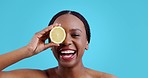 Skincare, lemon and black woman face with funny, smile and organic dermatology in studio. Blue background, happy female person and skin glow with fruit detox and health food with wellness shine