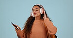 Dancing, phone and a student woman with headphones in studio for internet, backpack and song. Gen z person with a smartphone, singing and streaming or listening to music to relax on a blue background