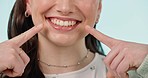 Woman, teeth and hand pointing closeup with cosmetics, dental hygiene and veneers in studio. Dentist work, female person face and happy from mouth wellness and tooth cleaning with blue background