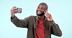 Peace, sign and man in selfie for social media, mockup and video call gesture with hand and phone on studio blue background. Influencer, emoji and smile for live stream, blog or profile picture pose