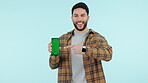 Happy man, face or green screen on a phone for social media advertising or online branding. Blue background, smile or portrait of person pointing to mobile app chroma key or mockup space in studio 