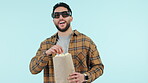 Face, smile and man with popcorn, movies and excited with glasses on a blue studio background. Portrait, happy person and model with eyewear, happiness and eating with film snack, watching a comedy
