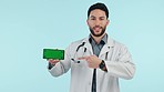 Doctor, phone green screen and pointing to healthcare information, presentation or speaking in studio. Face of medical man on mobile mockup, sign up choice and tracking marker on a blue background