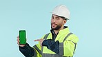 Construction man, green screen phone and studio with pointing, app promo or face by blue background. Engineer, maintenance employee or contractor for smartphone mockup, tracking markers or logo on ux