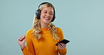 Woman, headphones and phone for music, dancing in studio with energy and fun isolated on blue background. Dancer, techno or EDM with audio streaming, mobile app and happiness, technology and internet
